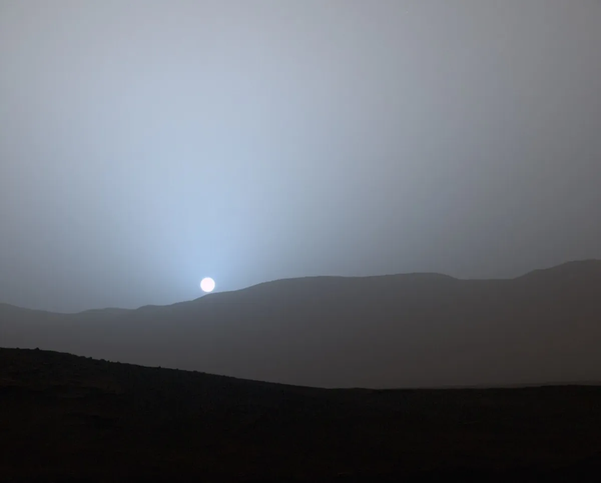 A blue glow around the Sun setting behind the rim of Gale Crater on Mars
